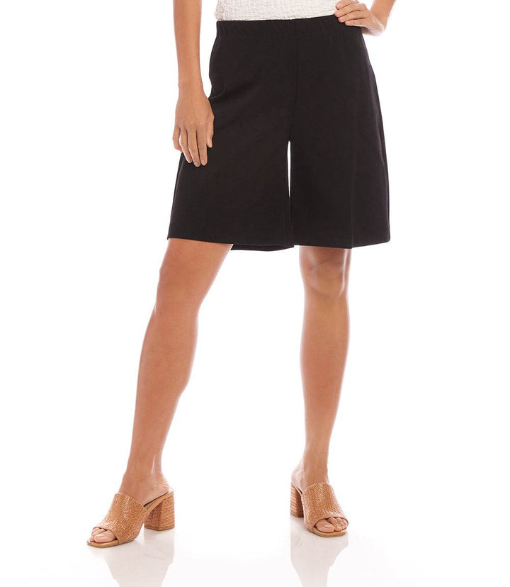 Woman wearing black high-rise A-line shorts made from double stretch twill with elastic waistband and mid-thigh length.