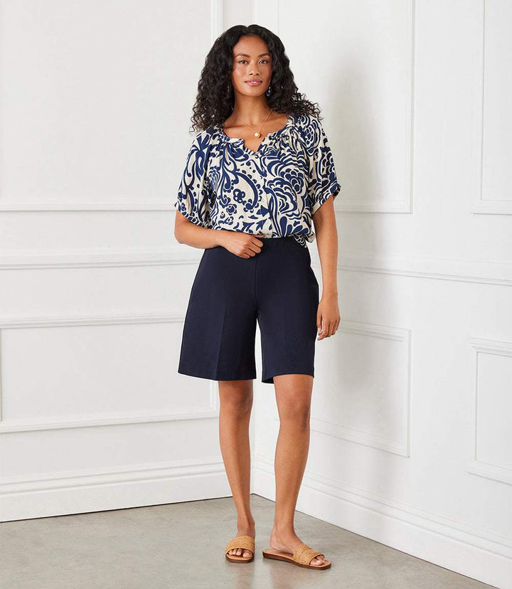 Woman wearing navy blue high-rise A-line shorts with elastic waistband and patterned blouse indoors