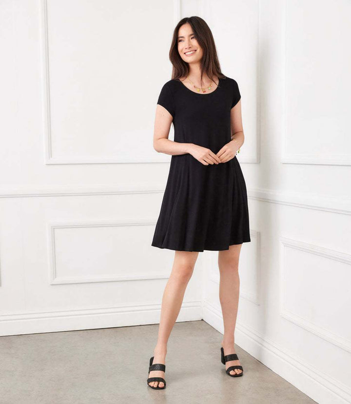 Woman wearing black Maggie Trapeze Dress with cap sleeves and boat neckline in a high-low hem style