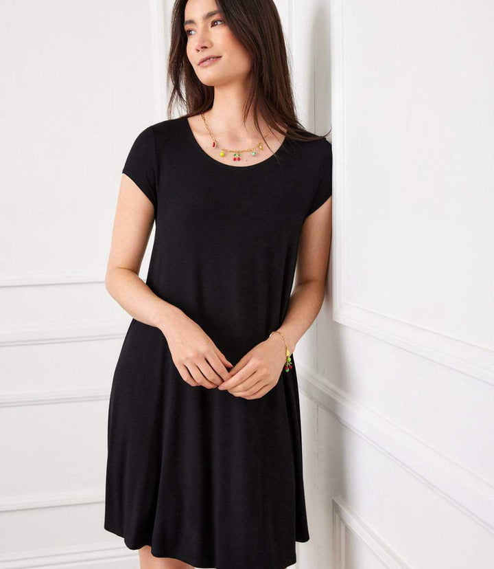 Woman wearing black Maggie Trapeze Dress with cap sleeves and boat neckline standing indoors