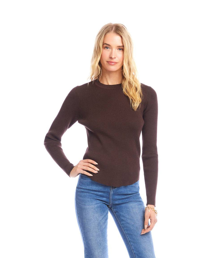 Woman wearing a fitted brown ribbed crewneck sweater with long sleeves and blue jeans