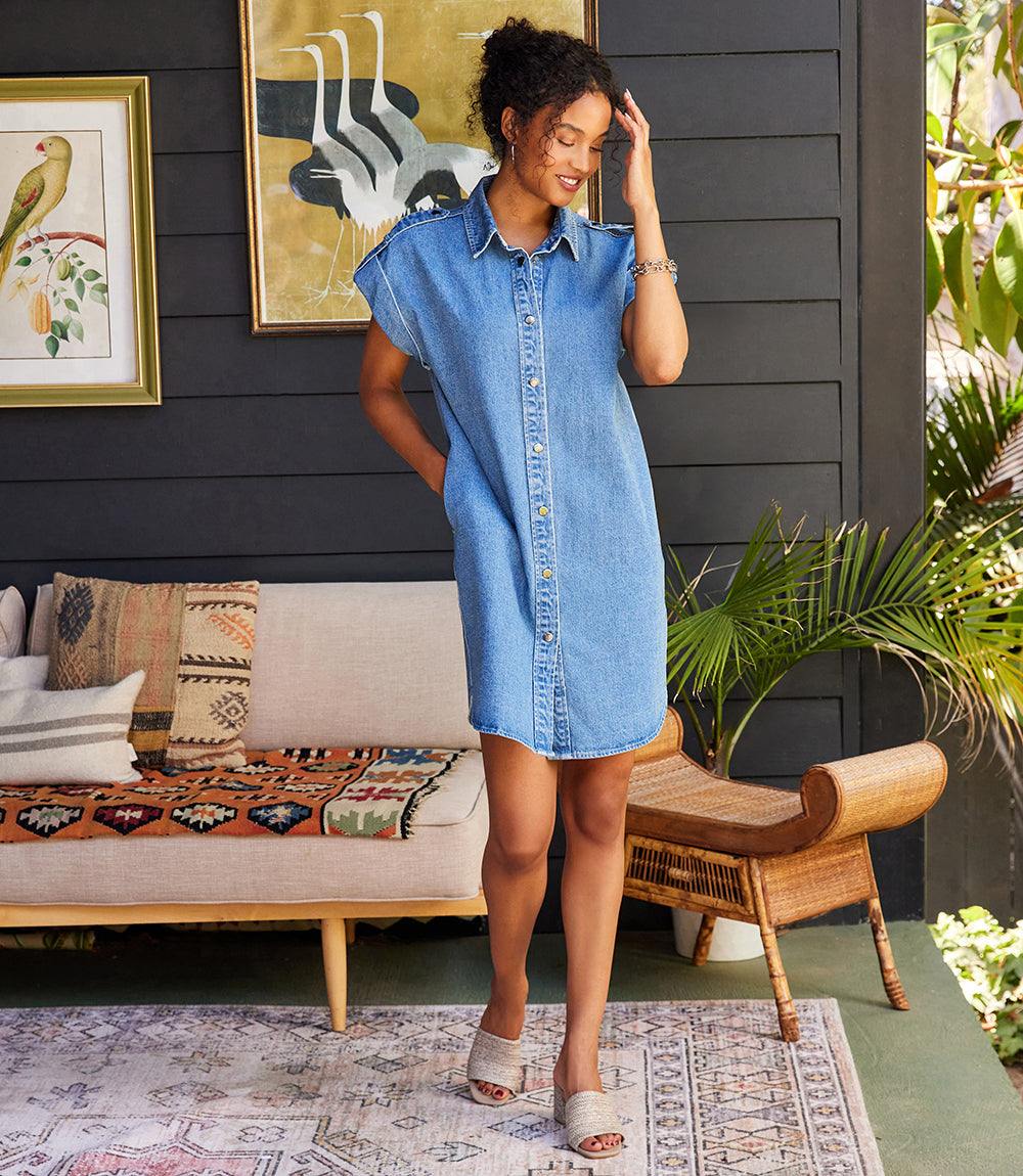 Woman wearing a cap sleeve denim shirtdress with front snap closure and collared neckline indoors