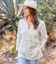 Woman wearing a white 3/4 sleeve embroidered tunic with tassel applique, bell sleeves, split neck, and side slits made of woven cotton.