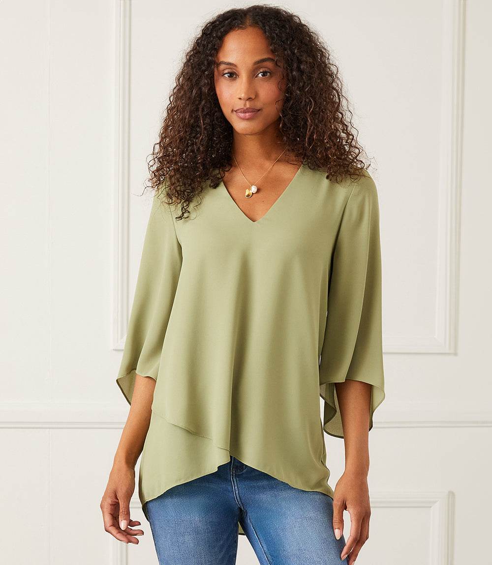 Woman wearing a light green Bracelet Sleeve Asymmetric Top with V-neck, flare sleeves, and layered asymmetrical hem paired with blue jeans.