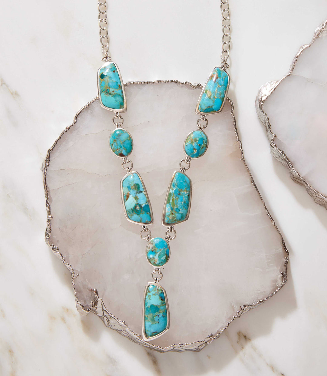 Turquoise stone statement necklace with sterling silver setting and varied shapes on a marble background