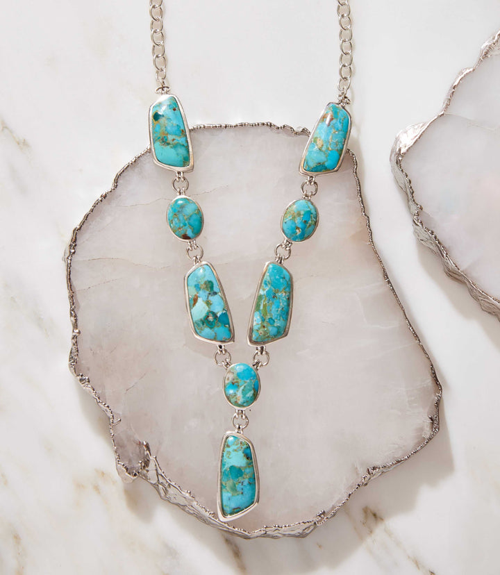 Turquoise stone statement necklace with sterling silver setting and varied shapes on a marble background