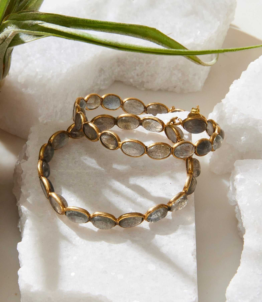 Gemstone hoop earrings with labradorite stones set in gold-plated brass hoops on white stone background