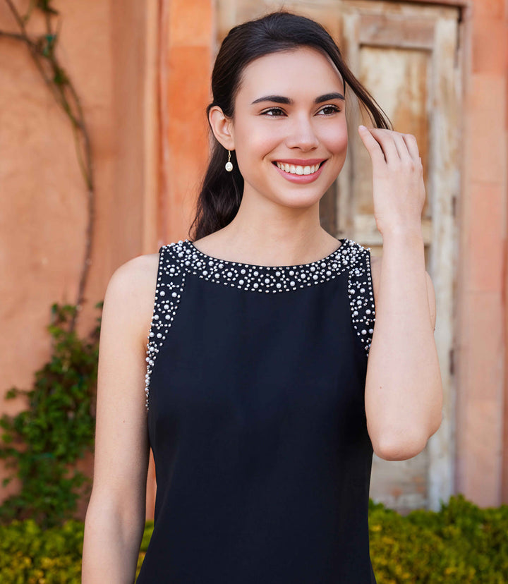 Woman wearing a black embellished sleeveless shift dress with boat neckline outdoors
