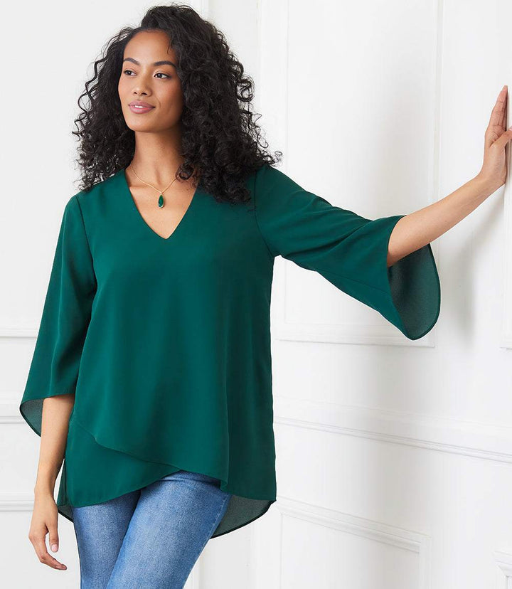 Woman wearing petite size green bracelet sleeve asymmetric top with V-neck and layered hem