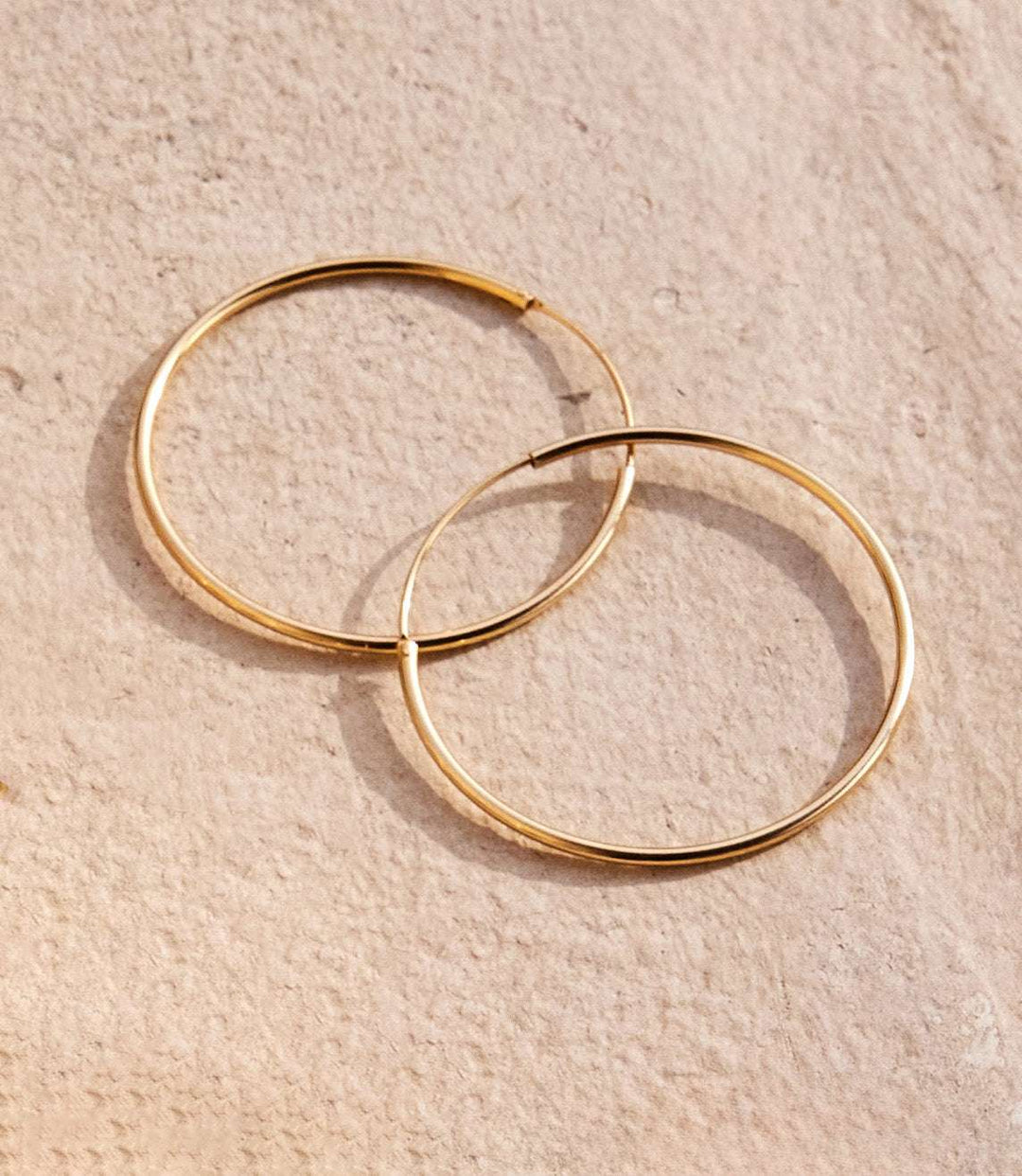 Large polished gold plated brass hoop earrings with 1.5 inch diameter and hidden post back design