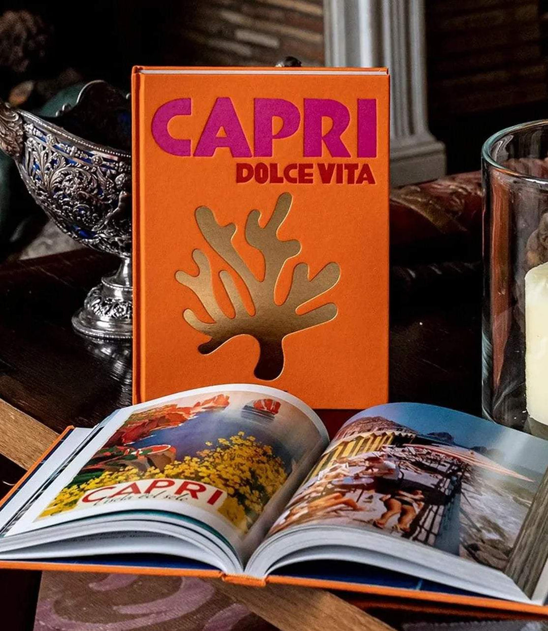 Capri Dolce Vita hardcover book with vibrant orange cover and gold coral design, opened to colorful island scenes