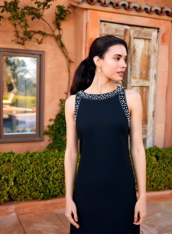 Woman in a black dress with silver embellishments standing outdoors.