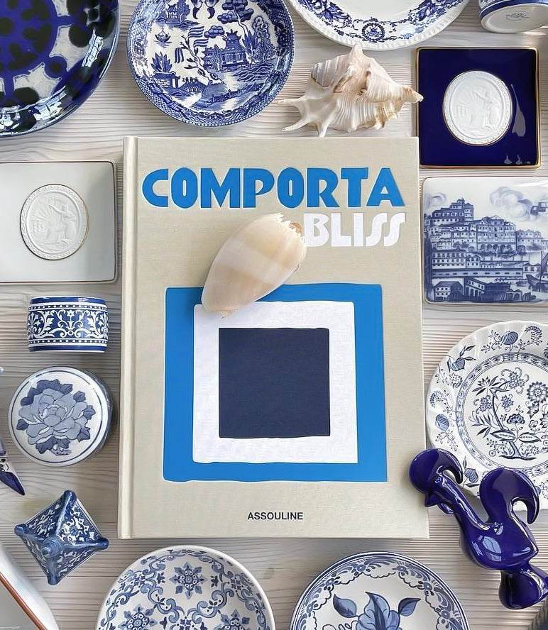 Comporta Bliss book surrounded by blue and white decorative plates and seashells on a white surface