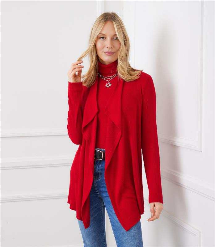 Woman wearing red long sleeve ribbed drape front cardigan with open front and high-low hem over a red turtleneck and blue jeans