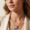Close-up of a woman wearing a colorful pendant necklace with a neutral background