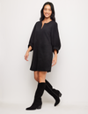 A woman modeling a black short puff-sleeve dress with a split neckline, paired with black knee-high boots, against a plain white studio background.
