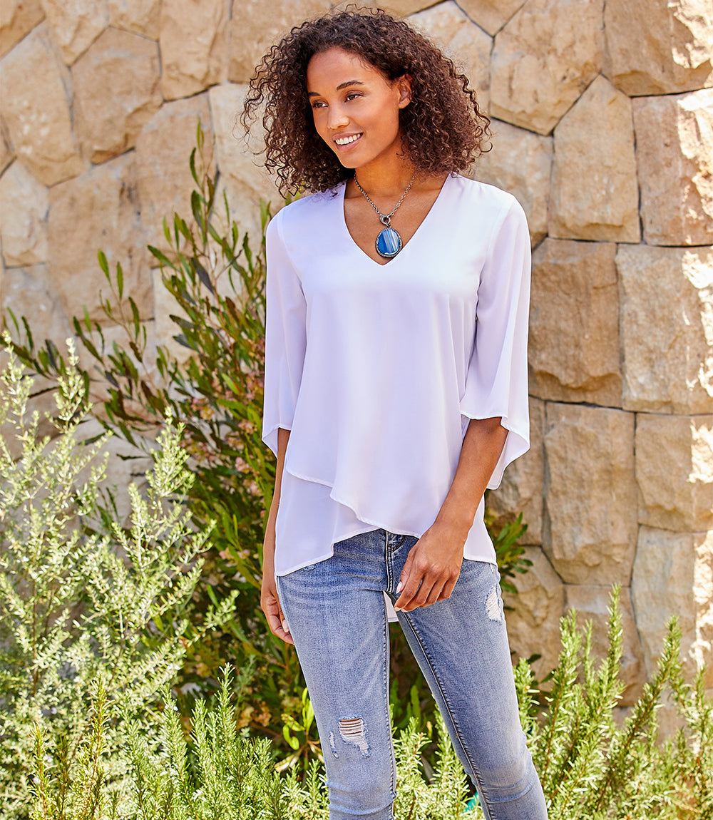 Petite size bracelet sleeve asymmetric top in silky crepe with layered hem and V-neck modeled outdoors