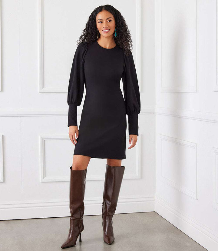 Petite size black bishop sleeve dress with wide cuffs and crew neck, fitted silhouette, worn with brown knee-high boots