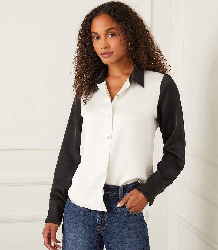 Woman wearing long sleeve satin colorblock shirt with white body and black sleeves and collar, button-down front, paired with blue jeans.