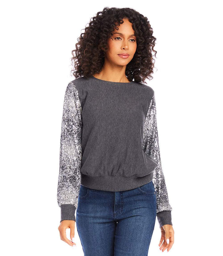 Woman wearing a dark gray sequin sleeve top with bishop sleeves and cuffed hem paired with jeans