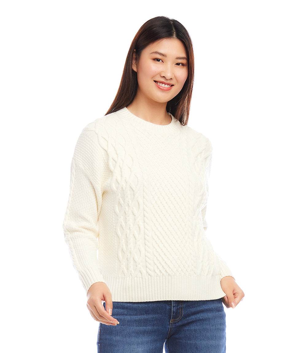 Woman wearing a petite size white chunky cable knit sweater with wide rib detail and dolman sleeves paired with blue jeans.