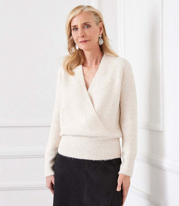 Woman wearing elegant cream wrap sweater with ribbed cuffs and hem, paired with black skirt