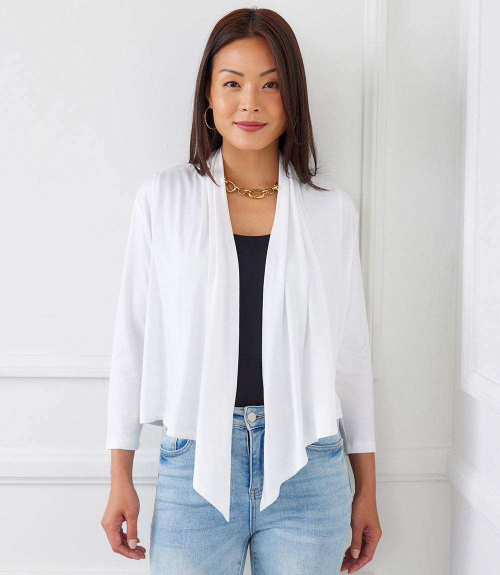 Woman wearing white Calli Cardigan with draped front and 3/4 length sleeves over black top and blue jeans