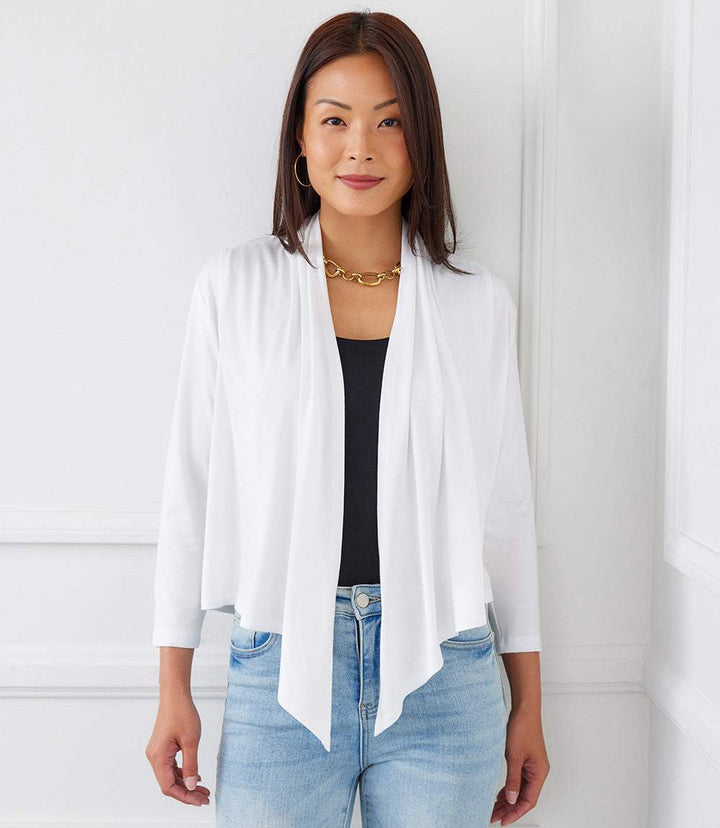 Woman wearing white Calli Cardigan with draped front and 3/4 length sleeves over black top and blue jeans