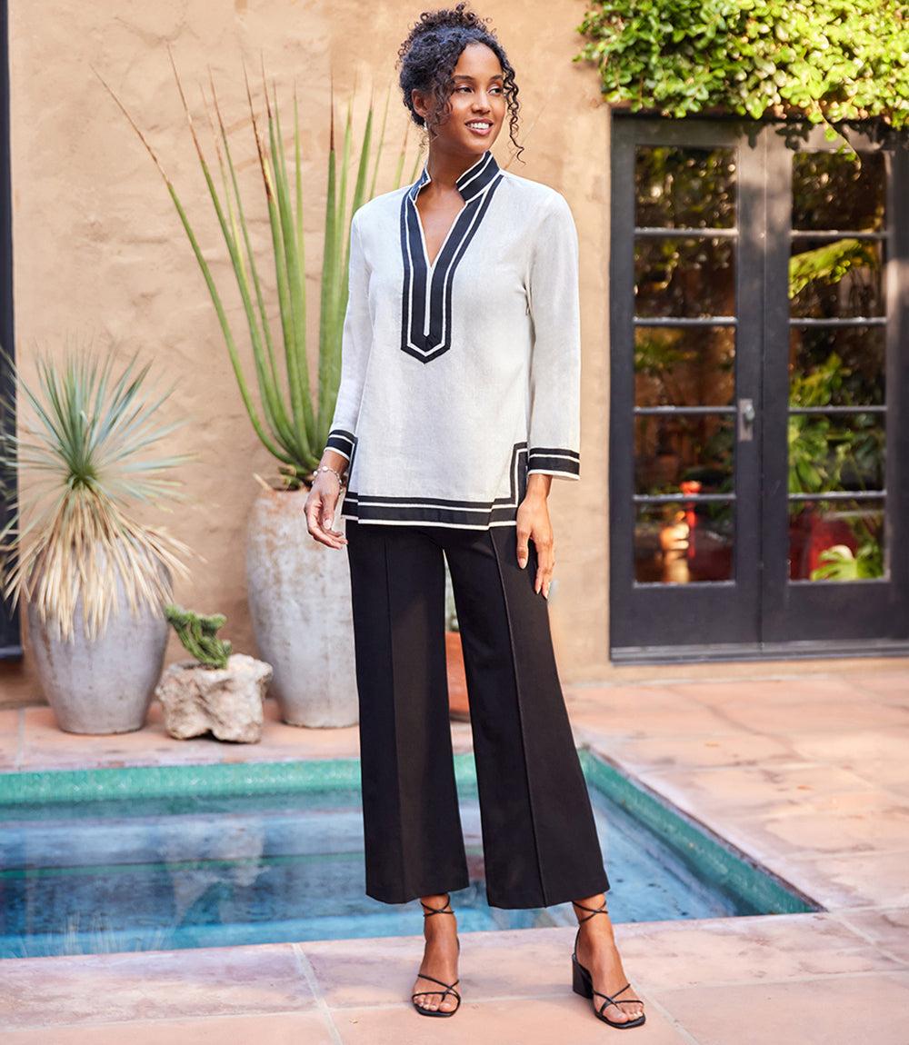 Woman wearing Petite Size The St. Tropez Tunic with mandarin collar and contrast trim, paired with black wide-leg pants and sandals near pool.