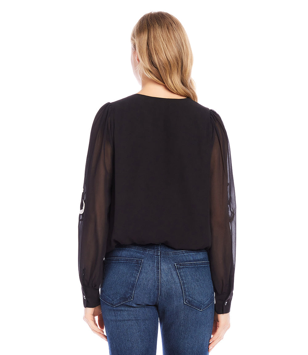 Back view of black embellished blouson top with sheer sleeves worn with blue jeans
