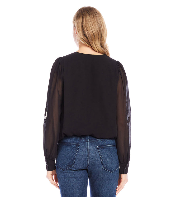 Back view of black embellished blouson top with sheer sleeves worn with blue jeans