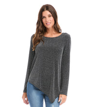 Woman wearing a long sleeve asymmetric hem top in shimmering knit fabric with boat neck and dark gray color
