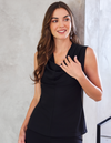A woman wearing a sleeveless black cowl-neck top with a peplum hem, posing against a textured gray wall.