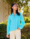 Woman wearing a light blue shirt and beige pants standing outdoors with greenery in the background