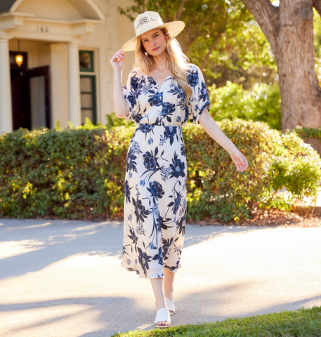 Woman in a floral dress and hat walking outdoors.