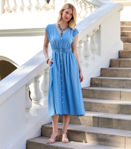Woman in a blue dress standing on stone steps with white railings.
