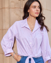 Woman wearing a light purple striped shirt with a beige wall background
