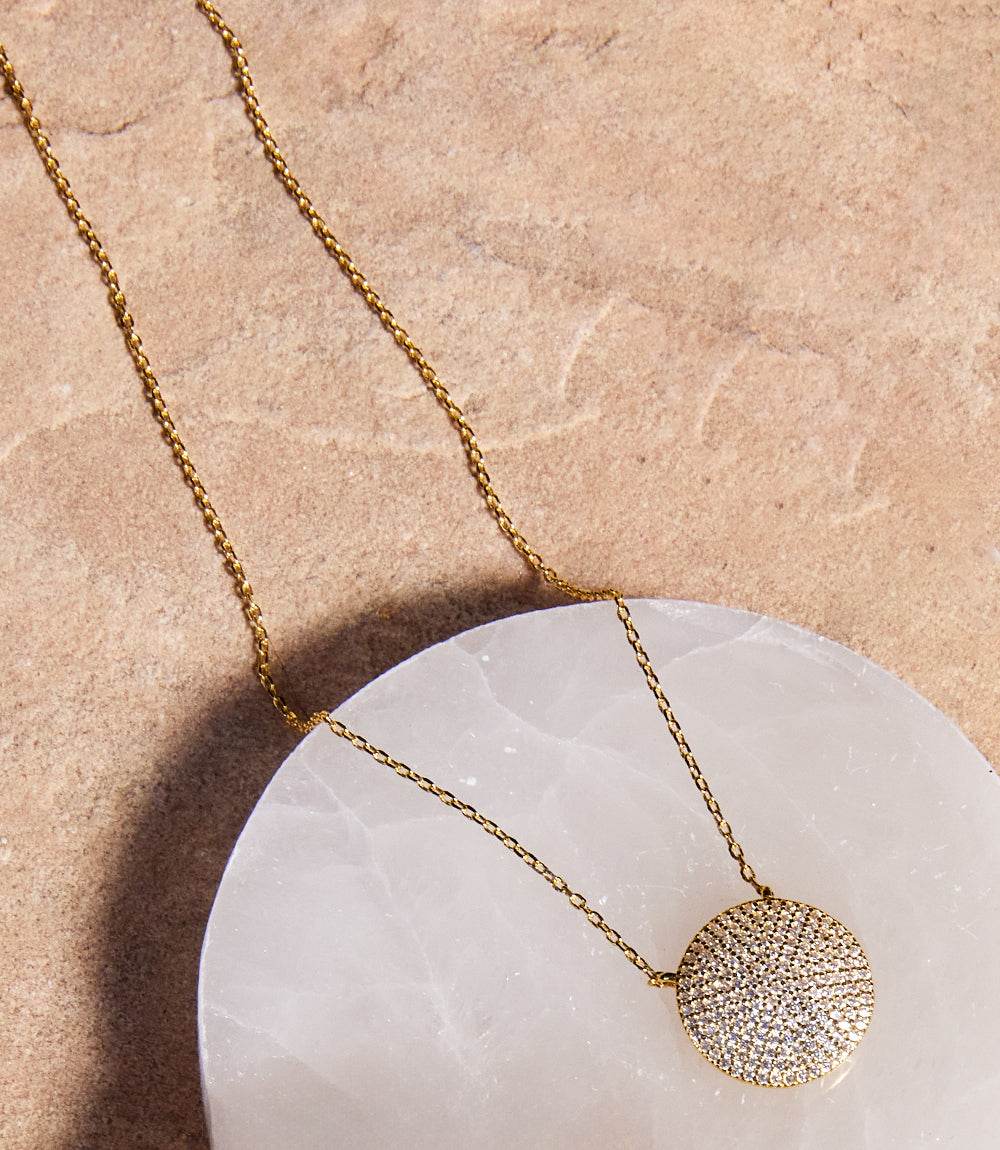 Gold plated sterling silver Pavé Disk Necklace with pavé crystals on a 16-inch chain with extender displayed on a white marble surface