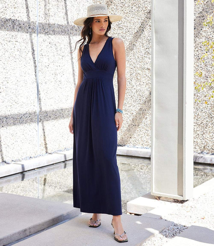 Woman wearing navy blue V-neck maxi dress with empire waist and sleeveless design outdoors