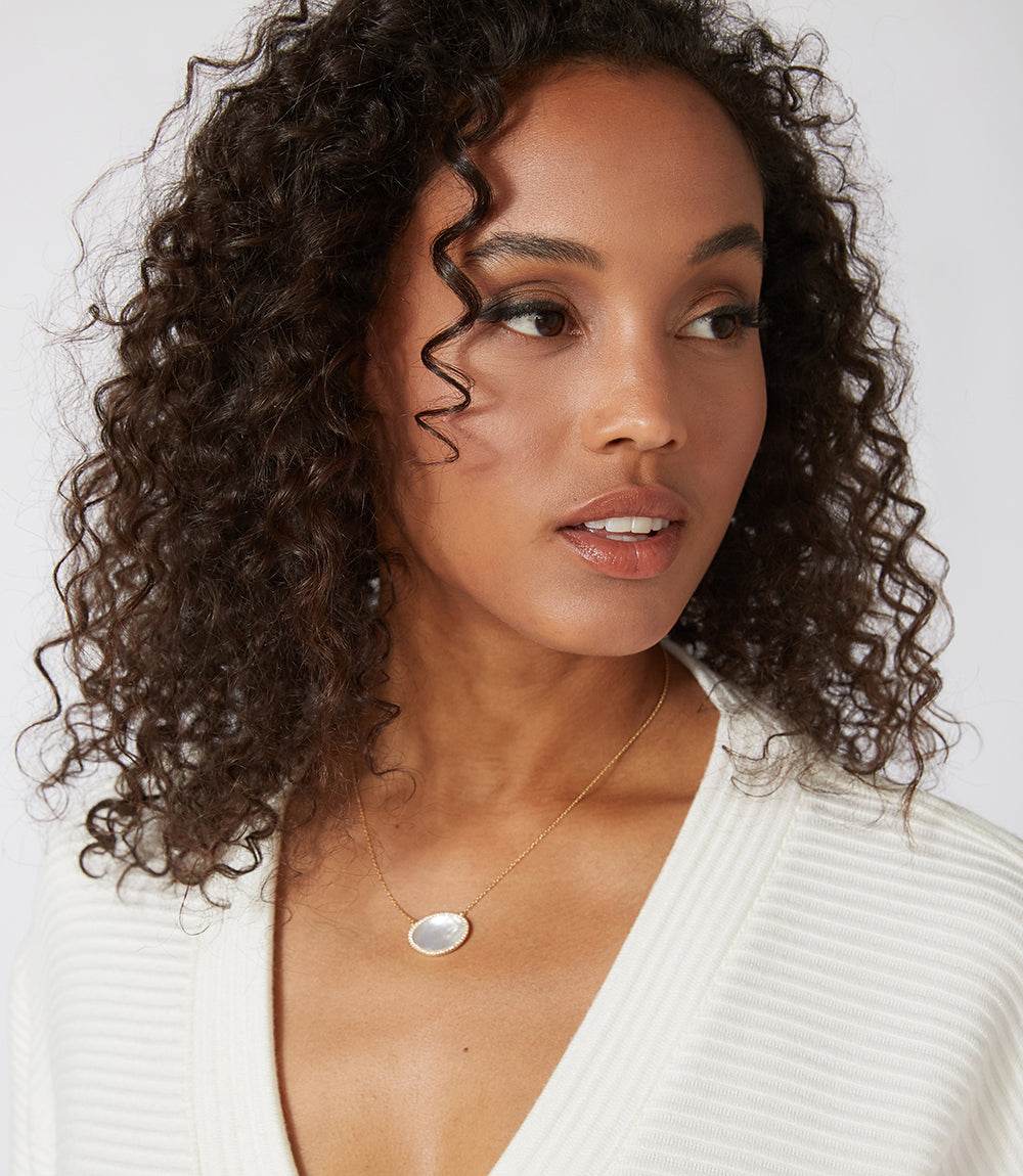 Woman wearing mother of pearl pendant necklace with 18K gold-plated chain and pavé crystal frame.