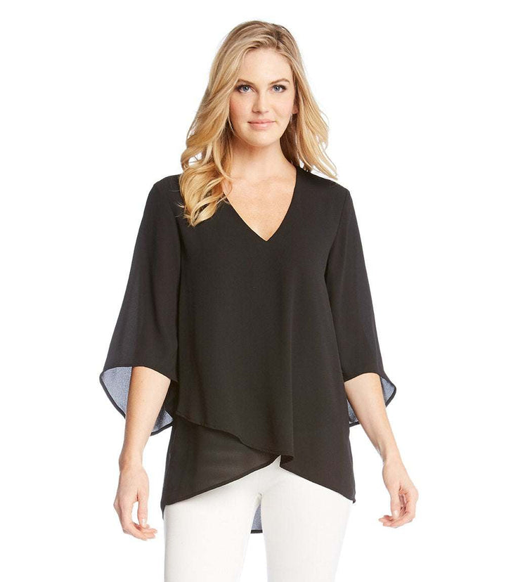 Woman wearing black bracelet sleeve asymmetric top with V-neck and layered hem paired with white pants