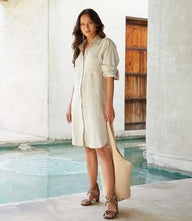 Woman wearing a petite size oatmeal linen shirtdress with roll-tab sleeves and front patch pocket standing by a pool.