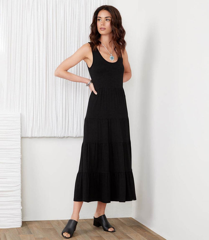 Woman wearing a black sleeveless tiered midi dress with scoop neckline and flouncy hem made from stretchy rayon spandex jersey.