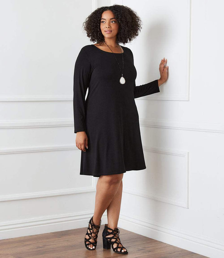 Plus size long sleeve black trapeze dress with scoop neckline and high-low hem modeled indoors