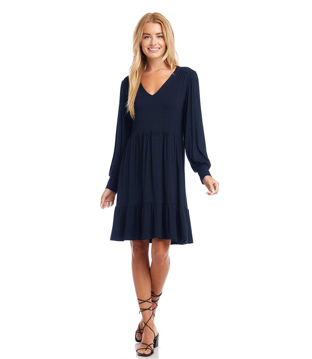Woman wearing a navy long sleeve tiered dress with V-neckline and blouson sleeves.